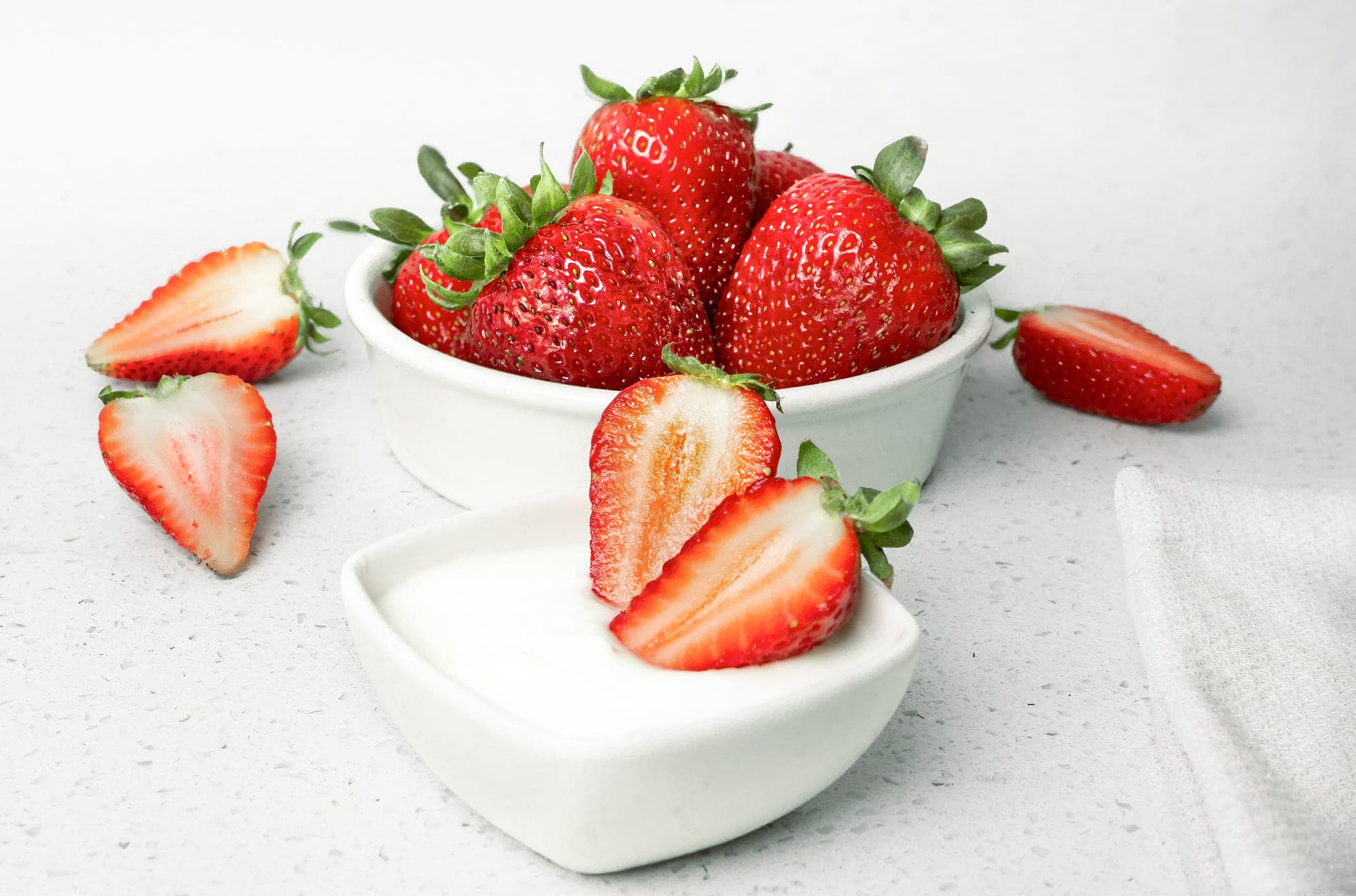 Frutillas en un bol blanco junto a un pocillo de yogur