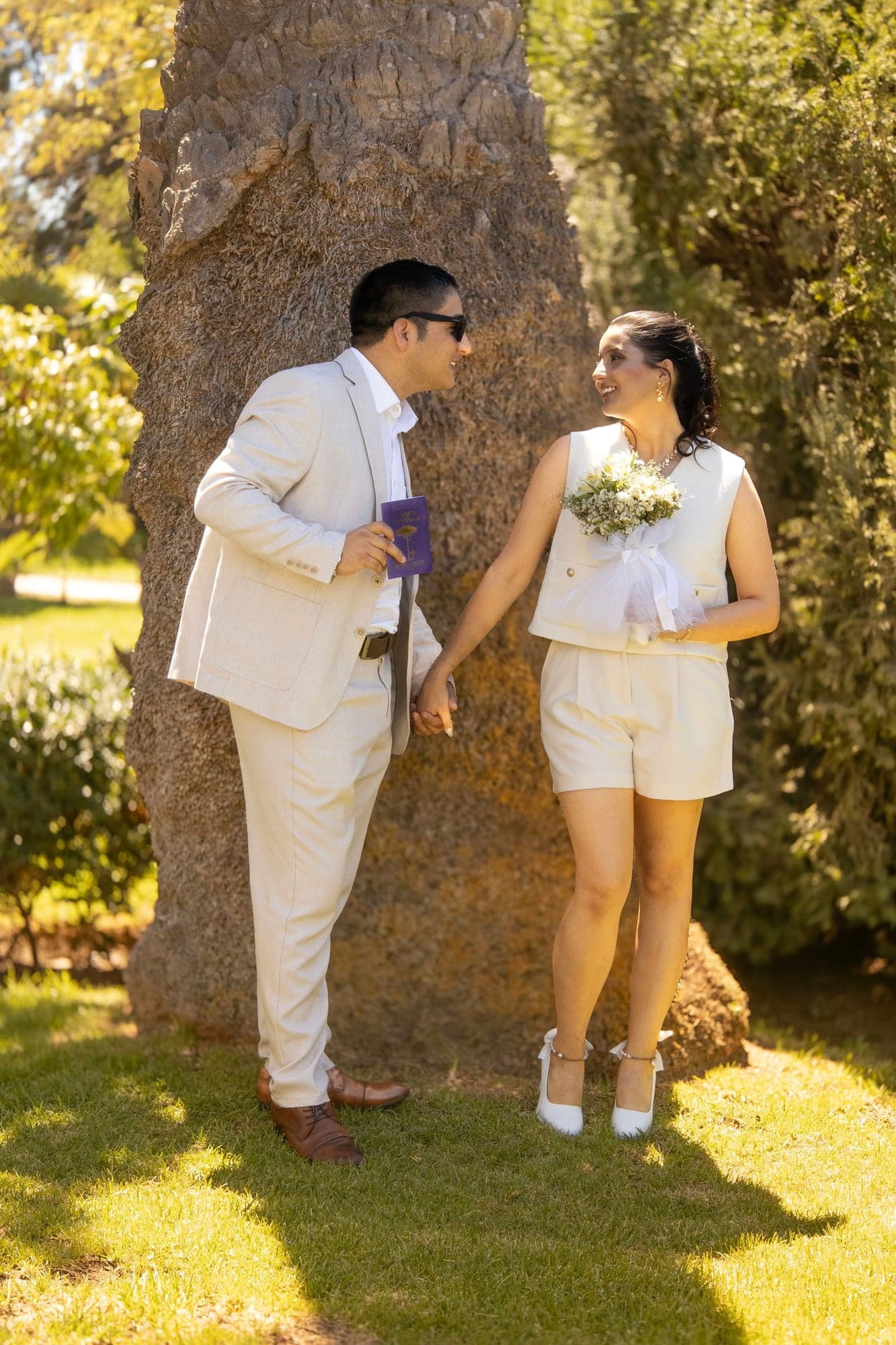 Novios se miran junto a un gran árbol en el jardín