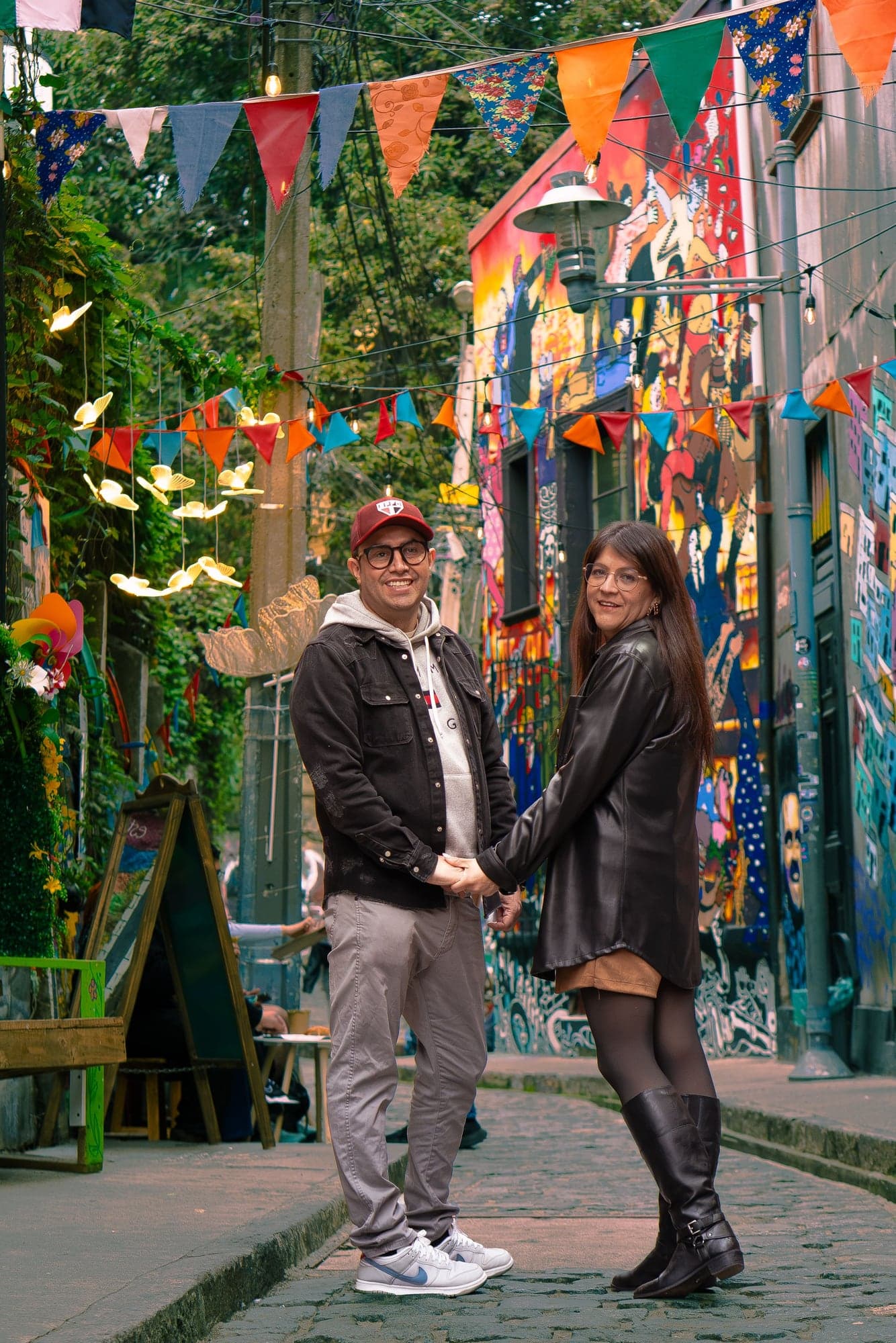 Valeska y Luis tomados de la mano en un pasaje con murales y banderines de colores